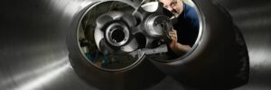 A man examines large metallic turbine parts through a cylindrical industrial machine in a workshop.